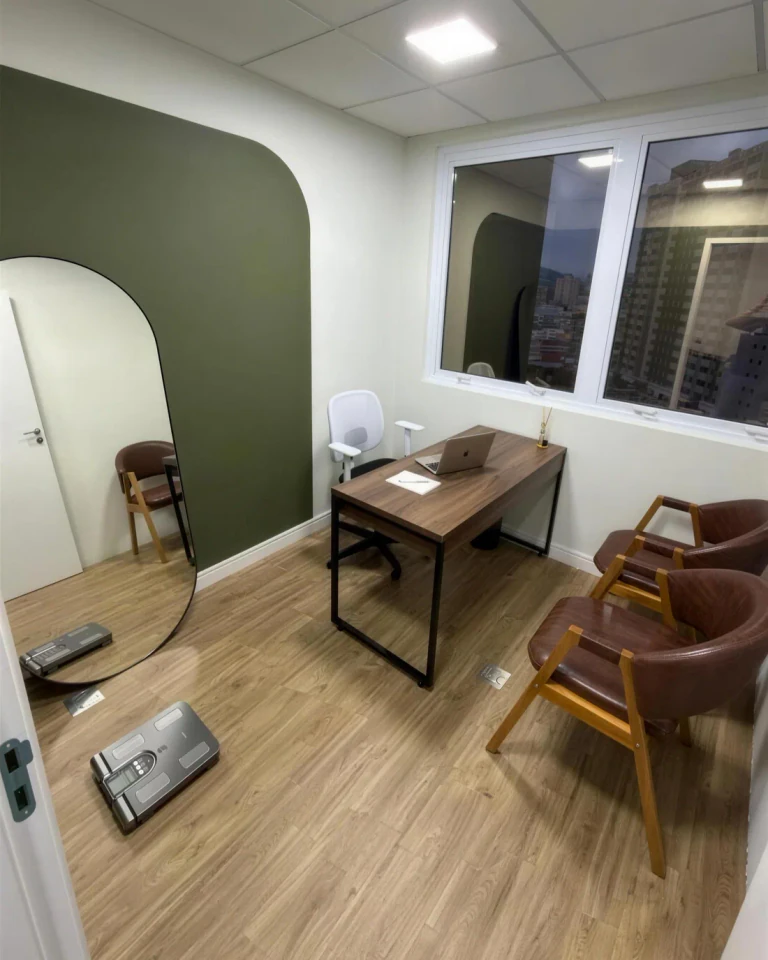 Sala de atendimento do consultório: parede oliva, mesa de madeira, poltronas e balança de bioimpedância no piso